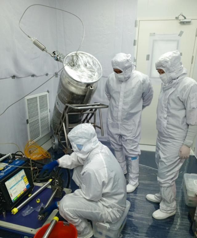 Cleanroom crew preparing a wrapped process canister for orbital welding beside the welder control unit