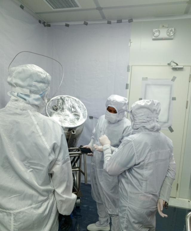 Gowned technicians setting up a wrapped process canister on its stand in the cleanroom