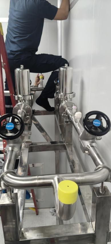 Gas panel skid with twin filter housings and Fujikin manual valves, with a technician working above it